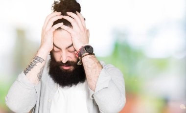 Genç adam uzun saçlı, sakallı ve küpe çünkü umutsuz ve stresli baş ağrısı acı acı ve migren. Ellerini kafasına.