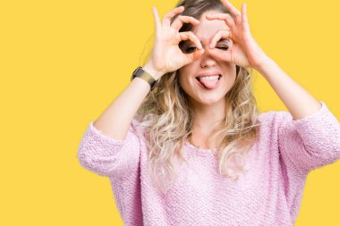 Güzel sarışın genç kadın dilini, parmaklarının arasından baktığını yapışmasını dürbün gibi ok jest yapıyor izole arka plan üzerinde. Deli ifade.