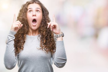 Güzel esmer kıvırcık saçlı Genç kız izole arka plan üzerinde bir kazak giyiyor hayret ve yukarıya bakıp parmakları ile işaret şaşırttı ve silah kaldırdı.