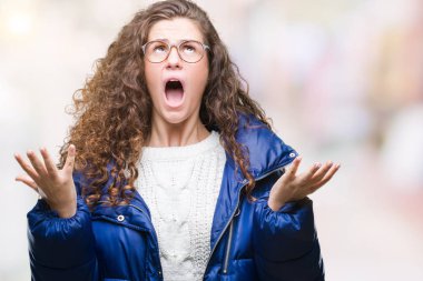 Güzel genç esmer kıvırcık saçlı kız izole arka plan çılgın ve kızgın bağırarak ve agresif ifade ve silah kaldırdı bağırmaya kış ceket, gözlük ve kazak giyiyor. Hayal kırıklığı kavramı.