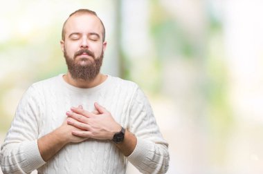 Göğüs kapalı gözlerle ellerinde ve yüzünde minnettar jest ile gülümseyen izole arka plan üzerinde kış kazak giyen genç beyaz hipster adam. Sağlık kavramı.