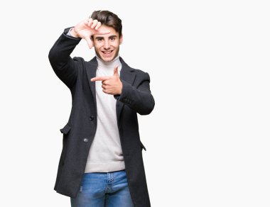 Genç zarif adam elleriyle yapım çerçeve ve parmakları ile mutlu yüz gülümseyen izole arka plan üzerinde kış palto giyiyor. Yaratıcılık ve Fotoğrafçılık kavramı.