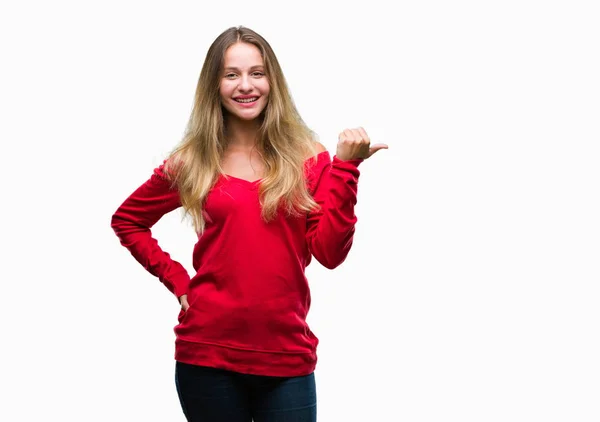 年轻美丽的金发碧眼的女人穿着红色毛衣在孤立的背景微笑着与快乐的脸看着和拇指指向的一侧 — 图库照片