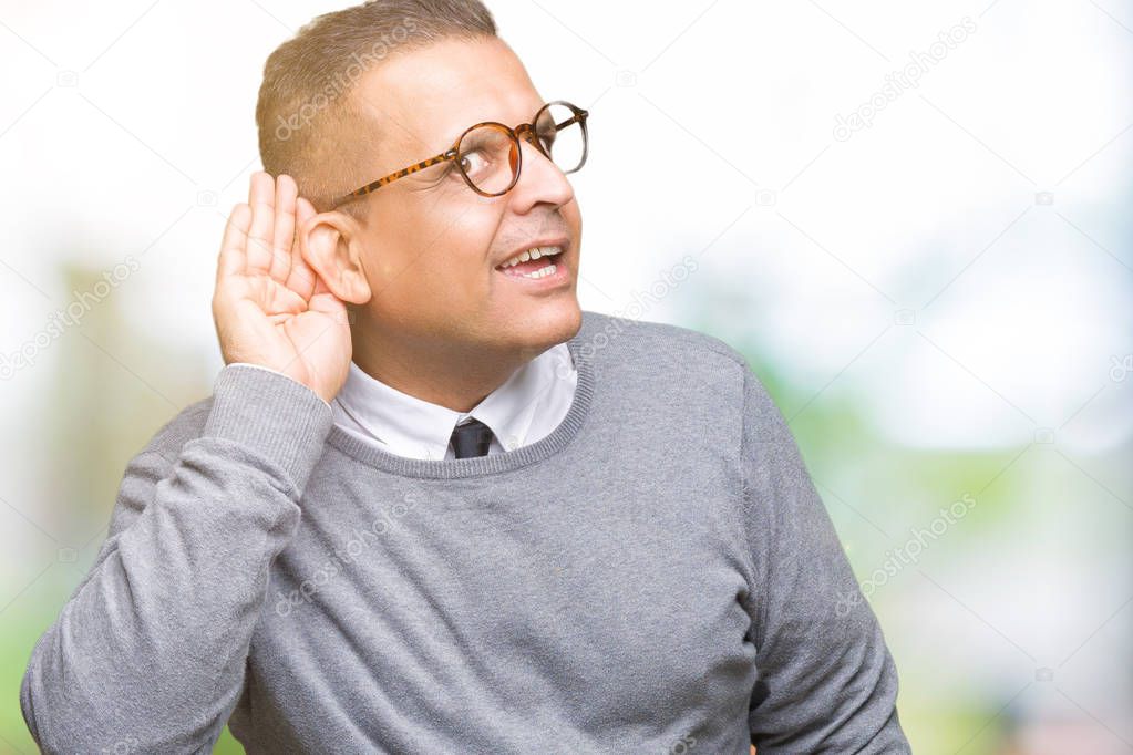 Middle age bussines arab man wearing glasses over isolated background smiling with hand over ear listening an hearing to rumor or gossip. Deafness concept.