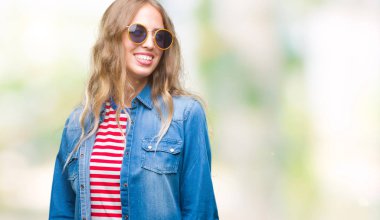 Güzel genç sarışın kadın uzak tarafına yüzünde, doğal ifade gülümseme ile seyir izole arka plan üzerinde güneş gözlüğü takıyor. Kendine güvenen gülüyor.