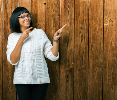 Güzel genç Afro-Amerikan kadın gülümseyerek ve iki elleri ve parmakları ile tarafına işaret kamera bakarak izole arka plan üzerinde gözlük.