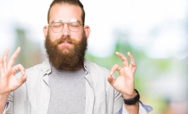 Genç sarışın adam gözlük rahatla ve gülümseyen gözlerle kapalı parmak jestle meditasyon yapıyor. Yoga kavramı.