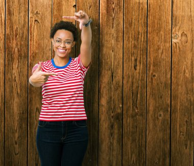 Elle yapma çerçeve ve parmakları ile mutlu yüz gülümseyen izole arka plan üzerinde gözlük güzel genç Afro-Amerikan kadın. Yaratıcılık ve Fotoğrafçılık kavramı.