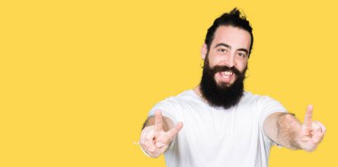 Uzun saç ve sakal casual beyaz t-shirt gülümseyen zafer işareti yapıyor parmak gösterilen kamera seyir giyen genç hipster adam. İki numaralı.