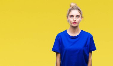 Yüzünde ciddi bir ifade ile izole arka plan üzerinde mavi t-shirt giyen genç güzel sarışın ve mavi gözlü kadın. Basit ve doğal kameraya bakıyor.