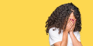 Yüzünü elleriyle ağlayarak süre kapsayan üzgün ifade ile beyaz t-shirt giyen kıvırcık saçlı Genç güzel kadın. Depresyon kavramı.