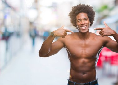 Çıplak vücut kendinden emin gösterilen ve işaret parmakları diş ve ağız ile gülümseyen izole arka plan üzerinde gösterilen Afro Amerikalı gömleksiz adam. Sağlık kavramı.