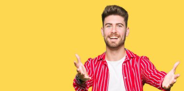 Sarılmak için kollarını açarak gülümseyerek kameraya bakarak kırmızı gömlek giymiş yakışıklı delikanlı. Neşeli ifade kucaklayan mutluluk.