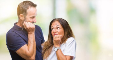 Orta yaş İspanyol rahat çift stresli ve gergin ile izole arka plan üzerinde tırnak ısırma dudaklarından eller. Anksiyete sorunu.