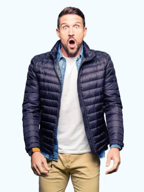 Yakışıklı adam korkuyor ve şok sürpriz ifade, korku ve heyecan yüz ile bir kış palto giyiyor.