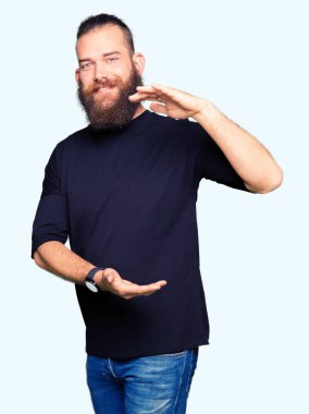 Büyük ve büyük boy işaret, ölçü birimi sembol gösteren elleriyle işaret rahat t-shirt giyen genç sarışın adam. Kameraya bakarak gülümsüyordu. Ölçüm kavramı.