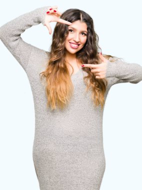 Elle yapma çerçeve ve parmakları ile mutlu yüz gülümseyen kış elbise giyen genç güzel kadın. Yaratıcılık ve Fotoğrafçılık kavramı.