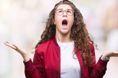 Güzel esmer kıvırcık saçlı Genç kız izole arka plan çılgın ve kızgın bağırarak ve agresif ifade ve silah kaldırdı bağırmaya ceket ve gözlük takıyor. Hayal kırıklığı kavramı.