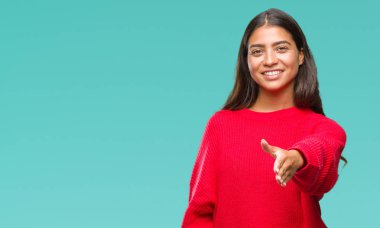 Üzerinde kış kazak giyen genç güzel Arap kadın arka plan dostu sunan karşılıklı tebrik ve davet edici gülümseyen izole. Başarılı iş.