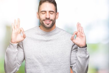 Genç yakışıklı adam giyen kazak izole arka plan üzerinde dinlenmek ve gülümseyen gözlerle parmak ile meditasyon jest yapıyor kapalı. Yoga kavramı.