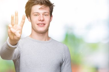 Gösterilen arka plan üzerinde kış kazak giyen genç yakışıklı adam izole ve parmakları ile işaret kendinden emin ve mutlu gülümseyerek iken üçüncü.