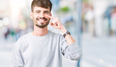 Genç yakışıklı adam giyen kazak izole üzerinden yüz ve burun, neşeli gülümseyerek el parmak ile işaret arka plan