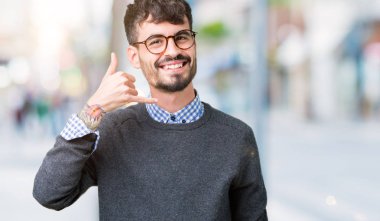 Genç yakışıklı yapıyor gülümseyen izole arka plan üzerinde gözlüklü adam akıllı telefon hareketi ile el ve parmak telefonda konuşuyor gibi. Kavramları iletişim.