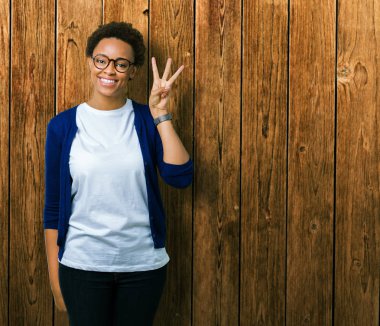 Genç güzel Afrikalı-Amerikalı kadın gözlük gösterilen ve parmakları ile işaret izole arka plan üzerinde ise kendinden emin ve mutlu gülümseyerek üçüncüsü.