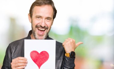 İşaret ve başparmak kadar mutlu yüz gülümseyen tarafı ile gösterilen Kırmızı kalp ile kağıt tutan yakışıklı orta yaş erkek
