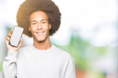 Ayakta ve diş gösterilen kendine güvenen bir gülümsemeyle gülümseyerek mutlu bir yüz ile akıllı telefon ekranını göstermeyi afro saçlı genç Afro-Amerikan adam
