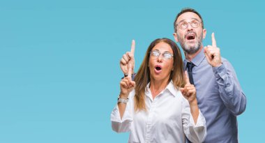 Orta yaş İspanyol çift izole arka plan üzerinde gözlük aşık hayret ve yukarıya bakıyor ve parmakları ile işaret ve silah kaldırdı şaşırttı.