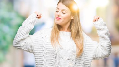 Genç güzel kadın rahat beyaz kazak kol kasları gururlu gülümseyen gösterilen izole arka plan üzerinde. Fitness kavramı.