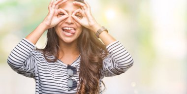 Genç güzel Arap kadın dilini, parmaklarının arasından baktığını yapışmasını dürbün gibi ok jest yapıyor izole arka plan üzerinde güneş gözlüğü takıyor. Deli ifade.