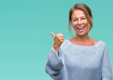 Seyir ve başparmak yanında yukarıyı mutlu yüz ile gülümseyen izole arka plan üzerinde kış kazak giyen orta yaş üst düzey İspanyol kadın.