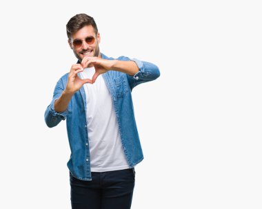 Genç yakışıklı adam aşık kalp simgesi ve elleriyle şekil gösteren gülümseyen izole arka plan üzerinde güneş gözlüğü takıyor. Romantik kavramı.
