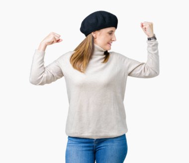Orta yaş Olgun kadın kol kasları gururlu gülümseyen gösterilen izole arka plan üzerinde kış kazak ve bere takıyor. Fitness kavramı.