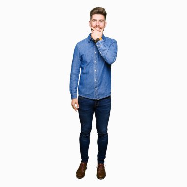 Emin çapraz kollar ve çeneme kaldırdı el ile gülümseme ile kameraya bakarak rahat kot gömlek giymiş genç yakışıklı sarışın adam. Pozitif düşünce.