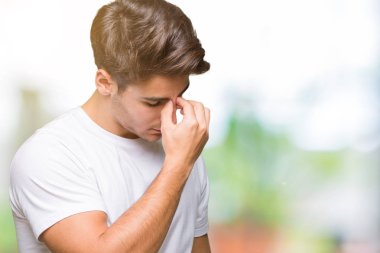 İzole arka plan yorgun sürtünme burun ve göz yorgunluğu ve baş ağrısı duygu üzerinde beyaz t-shirt giyen genç yakışıklı adam. Stres ve hayal kırıklığı kavramı.