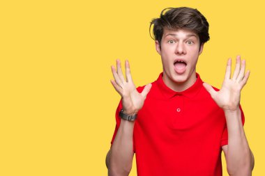 Üzerinde kırmızı t-shirt giyen genç yakışıklı adam deli kutluyor arka plan izole ve silah ile başarı için yükseltilmiş ve açık gözleri heyecanlı çığlık hayrete düşürdü. Kazanan kavramı