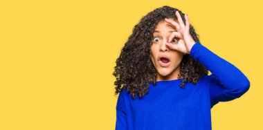 Sürpriz yüz, göz parmaklarının arasından seyir ile ok jest yapıyor kış kazak giyen kıvırcık saçlı Genç güzel kadın şok. İmansız ifade.