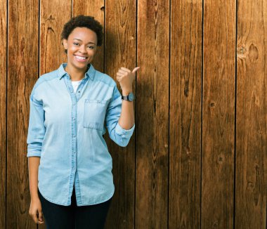 Seyir ve başparmak yanında yukarıyı mutlu yüz ile gülümseyen izole arka plan üzerinde genç güzel bir Afrikalı-Amerikalı kadın.