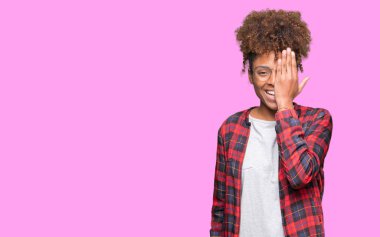 Güzel genç Afro-Amerikan kadın el yüz ve sürpriz duygu kendinden emin gülümseme ile tek gözüyle kapsayan izole arka plan üzerinde gözlük.