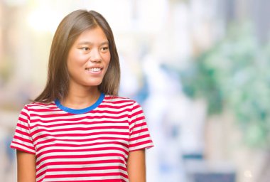 Genç Asyalı kadın uzak tarafına yüzünde, doğal ifade gülümseme ile seyir izole arka plan üzerinde. Kendine güvenen gülüyor.