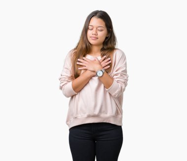 İle gülümseyen izole arka plan üzerinde pembe kazak giyen genç güzel esmer kadın kapalı gözler ve yüzünde minnettar jest ile göğüs üzerinde eller. Sağlık kavramı.