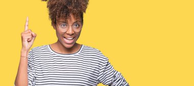 Başarılı fikirle izole arka plan işaret parmağı üzerinde gözlük takan güzel genç Afro-Amerikan kadın. Çıktıktan ve mutlu. Bir numara.