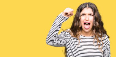 Giyen genç güzel kadın kazak öfkeli ve sinirli sinirli ve öfke ile bağırarak süre öfkeli yumruk yükselterek çizgili. Öfke ve agresif kavramı.