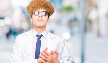 Profesyonel ceket ve ile gülümseyen güneş gözlüğü takan genç yakışıklı bilim adam kapalı gözler ve yüzünde minnettar jest ile göğüs üzerinde eller. Sağlık kavramı.