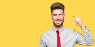 Gülümseyen genç yakışıklı iş adamı ve süre seyir ve kamera boyutu işaret parmaklarıyla yapıyor el ile kendine güvenen el hareketi. Ölçü kavramı.