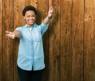 Sarılmak için kollarını açarak gülümseyerek kameraya bakarak izole arka plan üzerinde genç güzel Afrikalı-Amerikalı kadın. Neşeli ifade kucaklayan mutluluk.