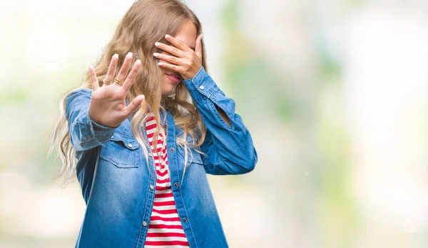 Beautiful young blonde woman over isolated background covering eyes with hands and doing stop gesture with sad and fear expression. Embarrassed and negative concept.